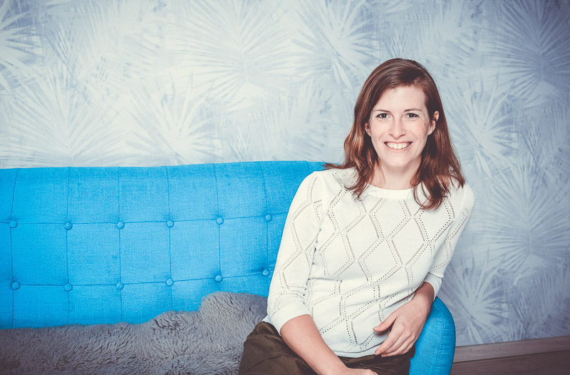 Eine Frau sitzt auf einem blauen Sofa und trägt einen weißen Pullover. Der Farbkontrast wirkt freundlich.