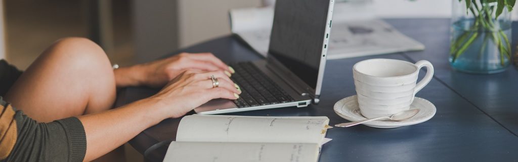 Eine Frau sitzt gemütlich mit verschränkten Beinen am Tisch und am Laptop an einem Text.