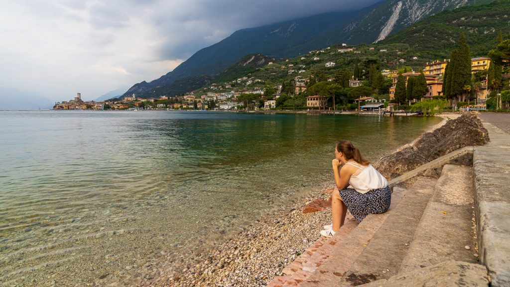 Eine Frau sitzt am Gardasee und blickt auf die Burg von Malcesine.