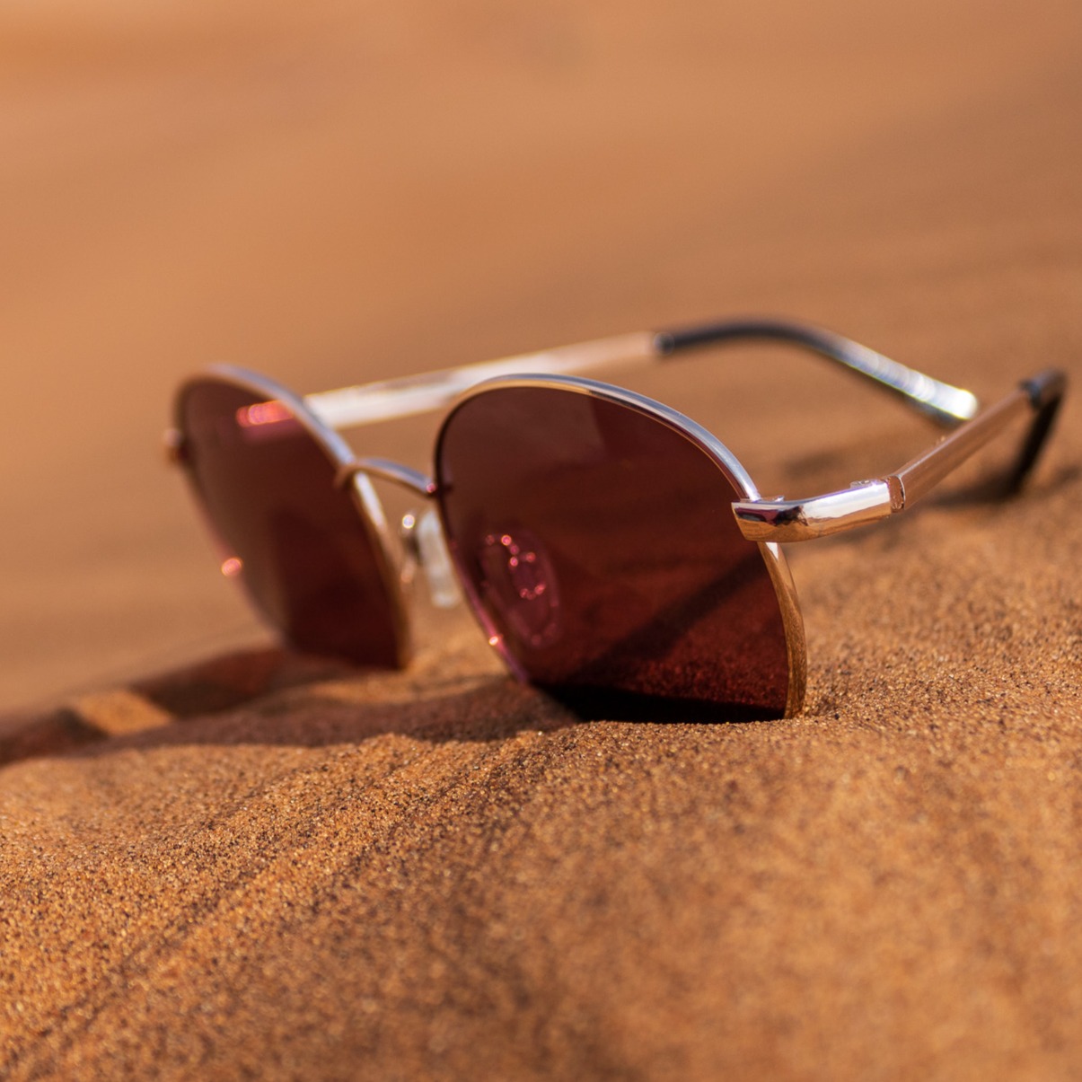 Eine rot getönte Sonnenbrille liegt im Sand.